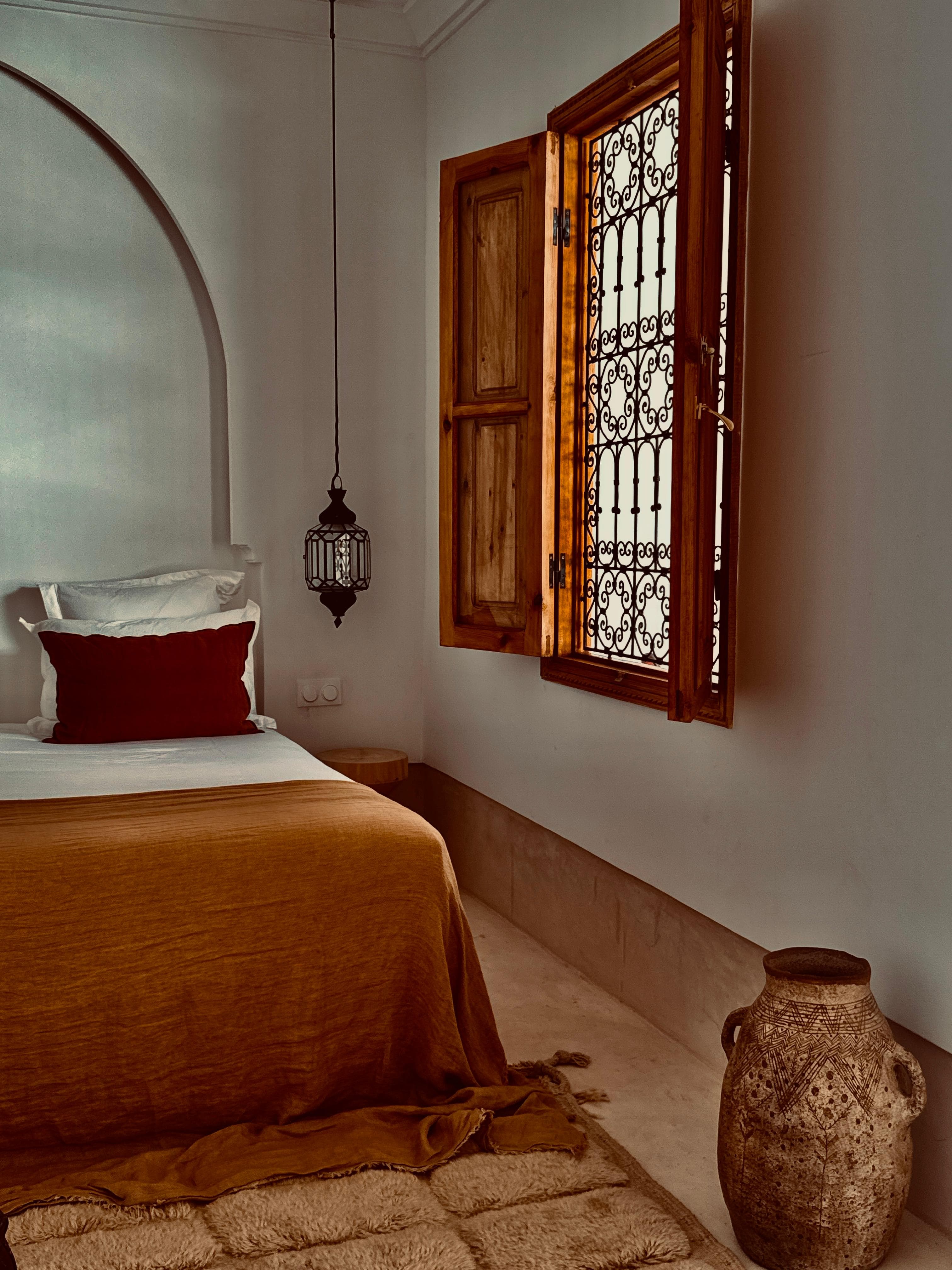 La chambre achevée, lit habillé de lin terracotta et fenêtre en fer forgé.